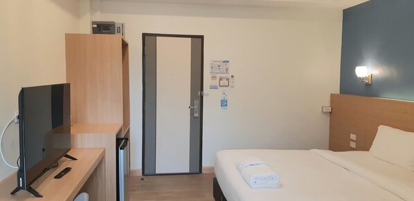 Habitación de hotel con cama, un televisor sobre un escritorio de madera, una puerta y una lámpara fijada a la pared.