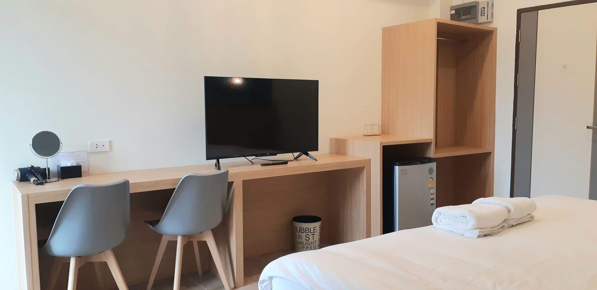 Una habitación de hotel con una cama, un escritorio con televisor, dos sillas, un microondas y un cubo de basura.