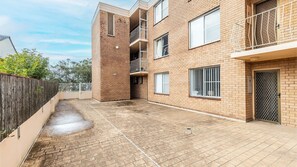 Un immeuble à plusieurs étages, construit en briques, doté de balcons, d’une entrée fermée par un portail et d’une cour dallée.