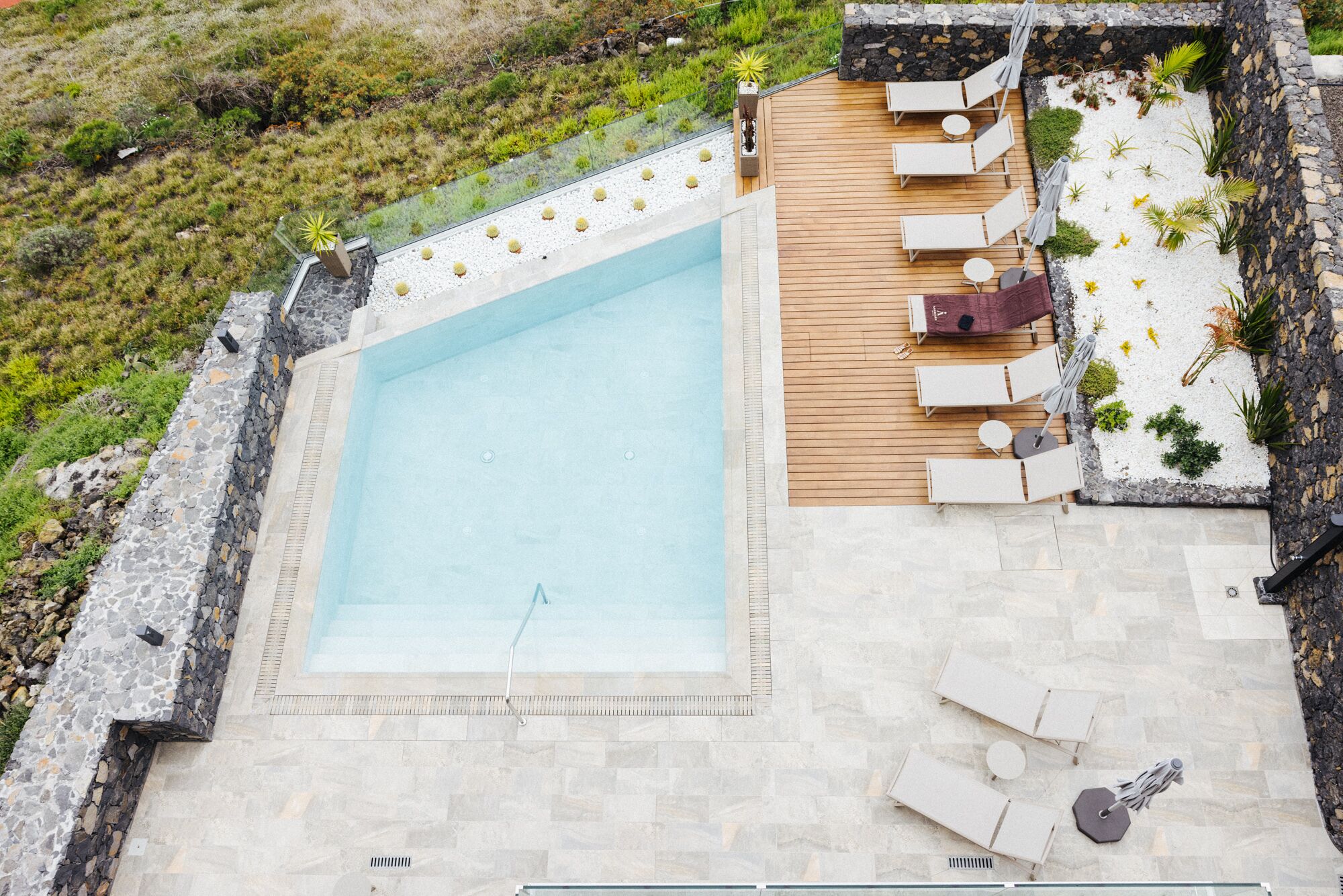 A rectangular swimming pool with a wooden deck and lounge chairs.