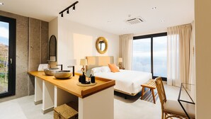Une chambre d’hôtel moderne avec un grand lit, un bureau en bois, un fauteuil en osier et une vue sur la ville.
