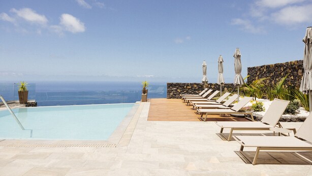 Un espace aménagé au bord de la piscine, avec des chaises longues et des parasols, offrant une vue imprenable sur l’océan.