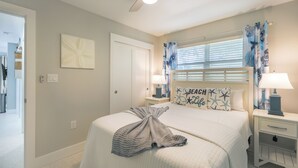 Une chambre à coucher avec un lit, un ventilateur de plafond, une table de chevet avec une lampe et une fenêtre avec des rideaux.
