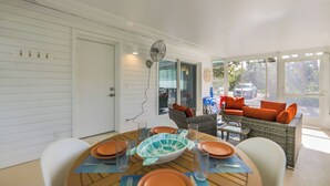 Un coin repas avec une table dressée pour quatre personnes, un canapé en osier avec des coussins orange et un ventilateur au plafond.