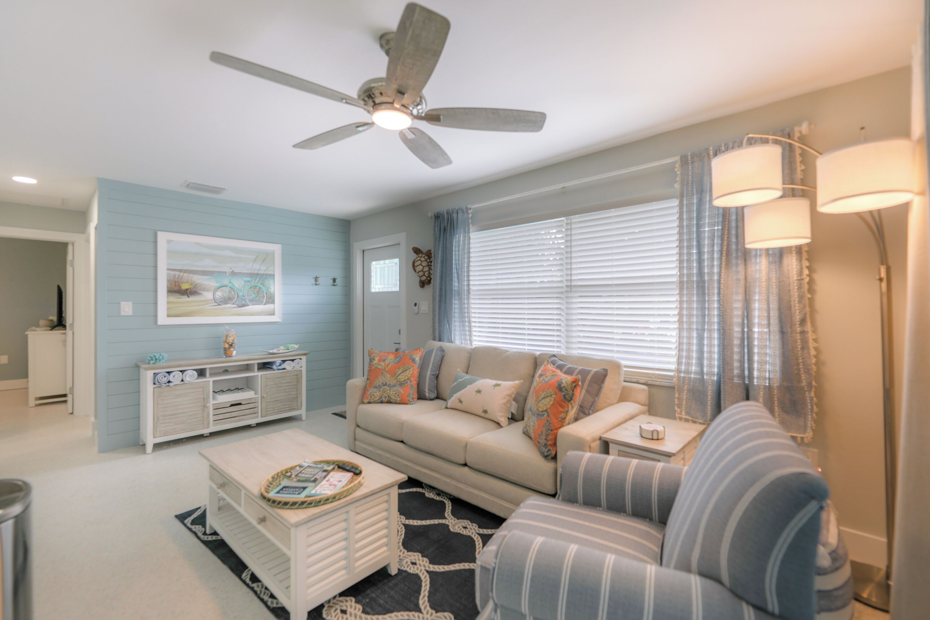 A living room with a sofa, a coffee table, a ceiling fan, and a window with blinds.