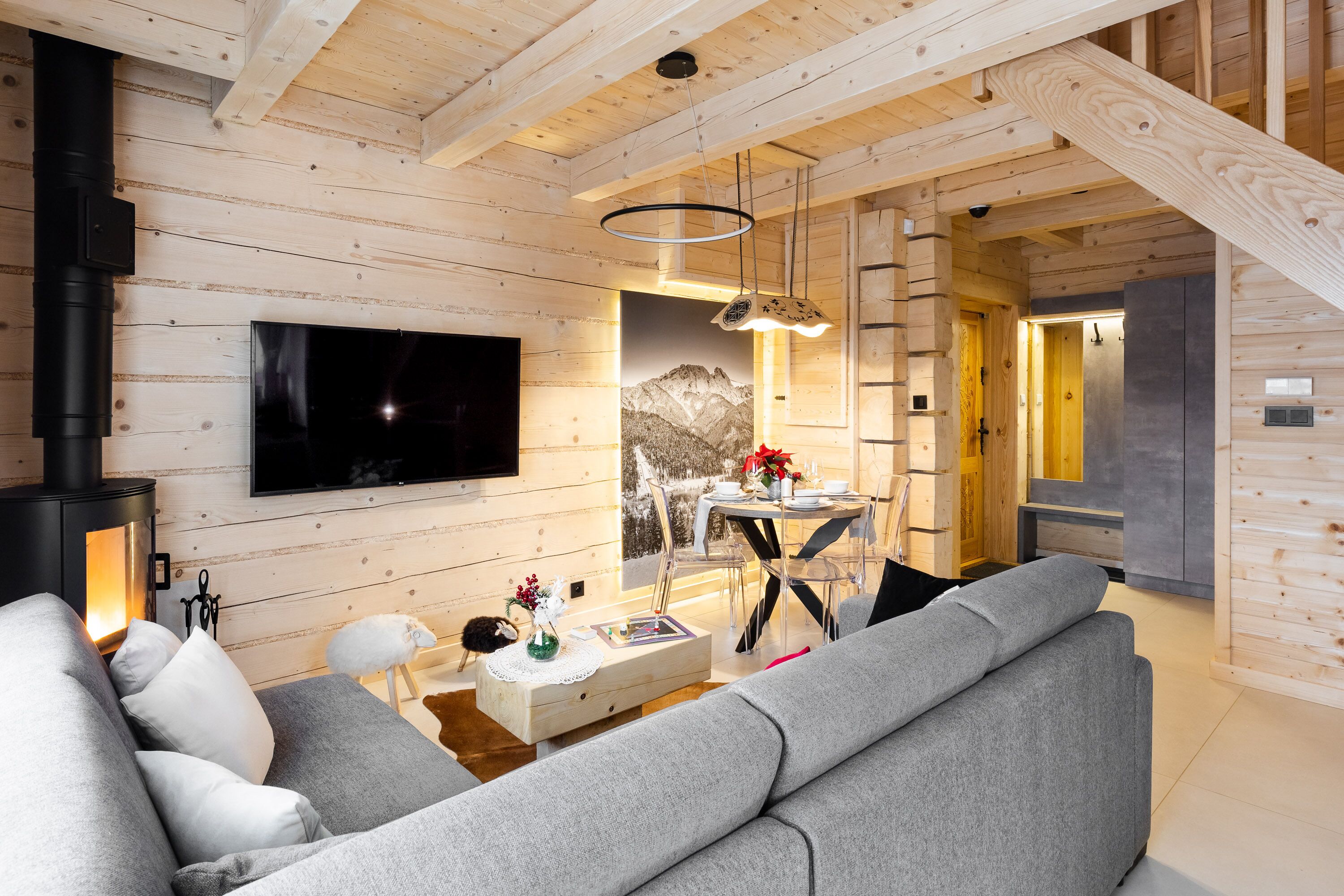 A cozy log cabin interior with a fireplace, a mounted TV, a dining area, and a modern sofa.