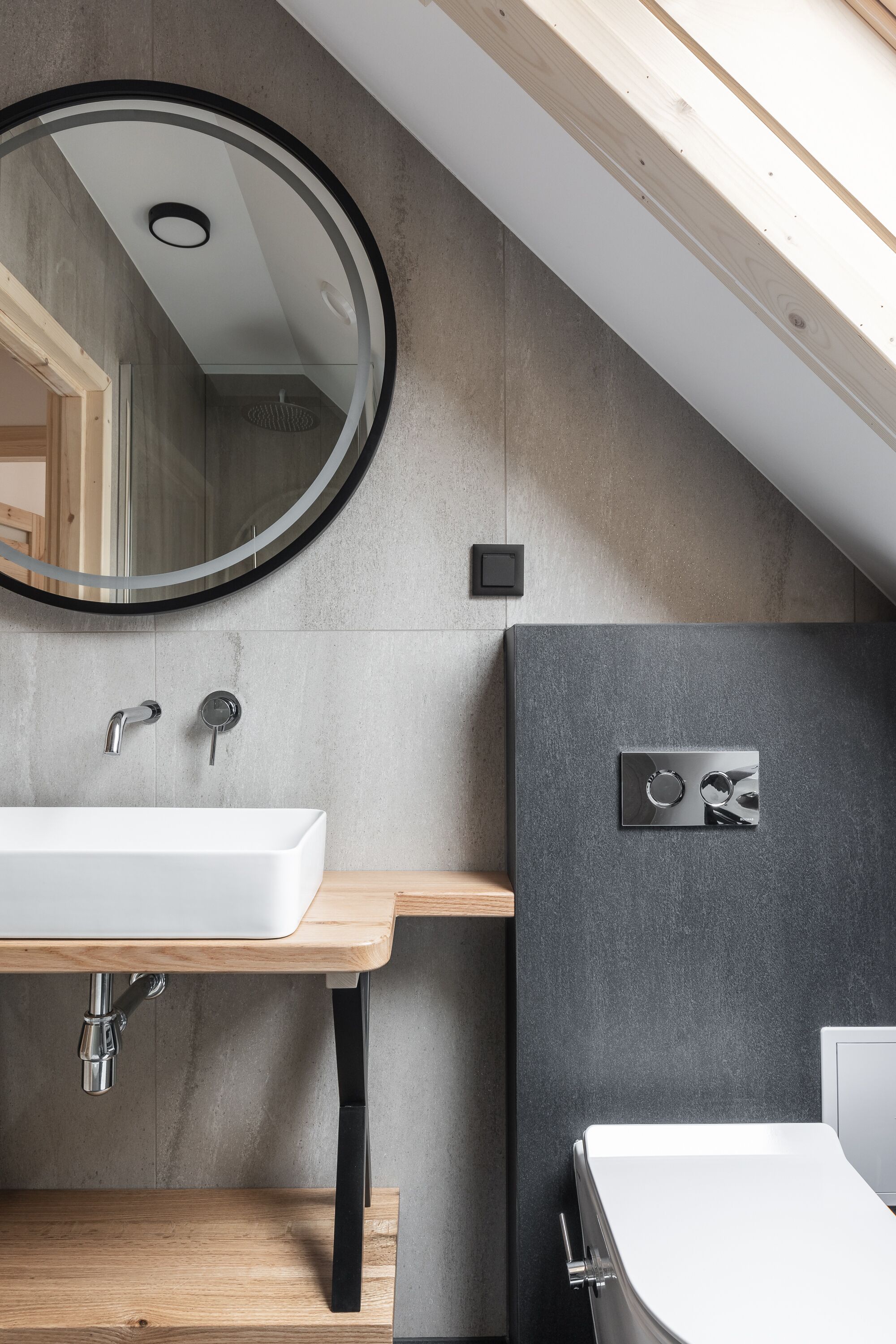 Un baño moderno con un lavamanos rectangular, un espejo redondo y una zona de ducha.
