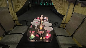 A table set for a meal with candles and flowers, surrounded by chairs. - Heaven7 Hotel & Resort (Himatnagar)