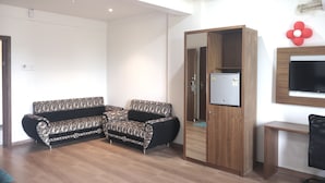 A living room with a sofa, a wooden cabinet, and a TV mounted on the wall. - Heaven7 Hotel & Resort (Himatnagar)