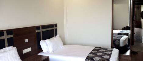 A hotel room with two single beds, a wooden headboard, a mirror, and a wardrobe.