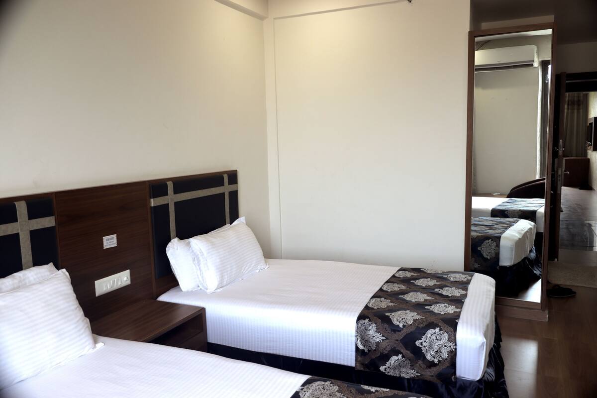 A hotel room with two single beds, a wooden headboard, a mirror, and a wooden floor.