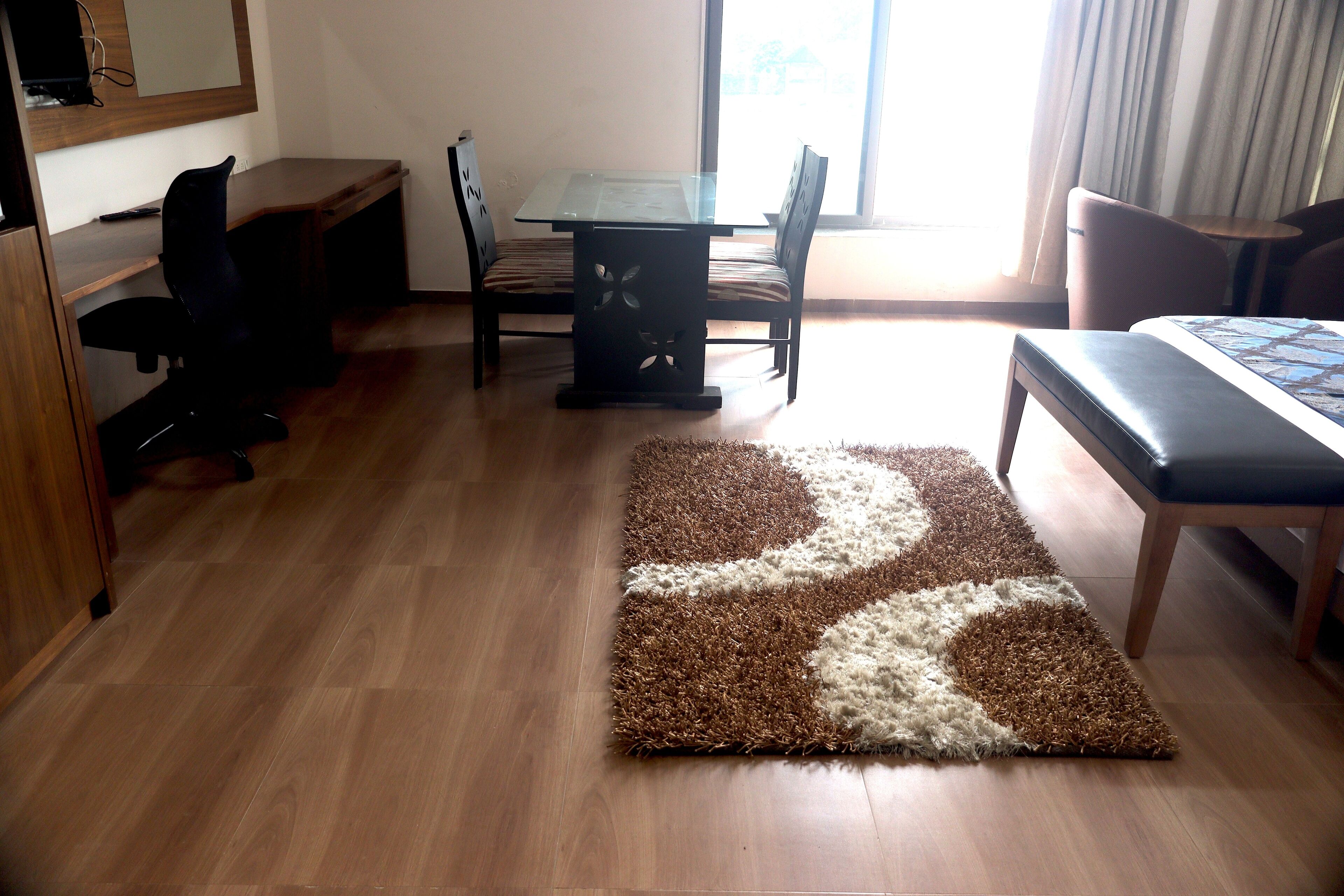 A hotel room with a wooden desk, two chairs, a small table, a bed, and a patterned rug.