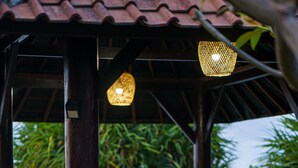 Ein Holztisch und Stühle unter einem Vordach mit hängenden Lampen, mit Blick auf einen Strand.