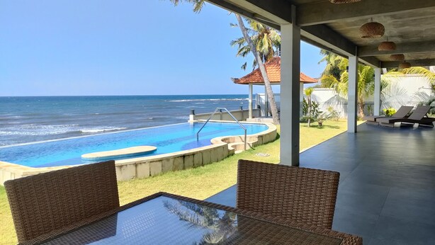 Ein Pool mit Blick auf das Meer, Korbmöbel und ein überdachter Bereich mit hängenden Lichtern.
