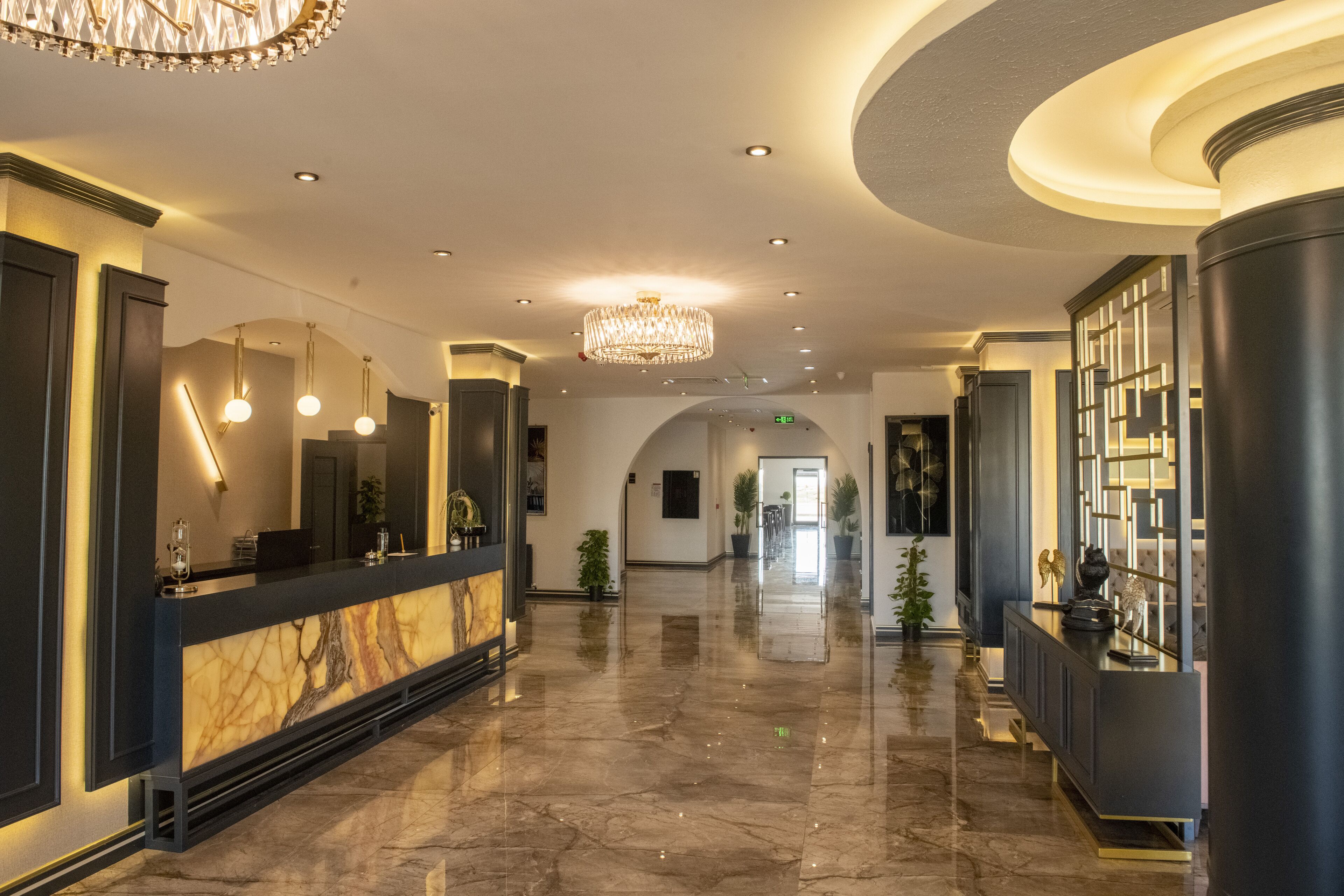 Un vestíbulo amplio con un mostrador de recepción de mármol, candelabros modernos y un piso limpio y pulido.