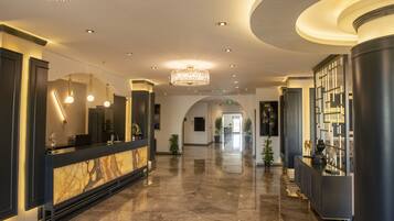 Un vestíbulo amplio con un mostrador de recepción de mármol, candelabros modernos y un piso limpio y pulido.