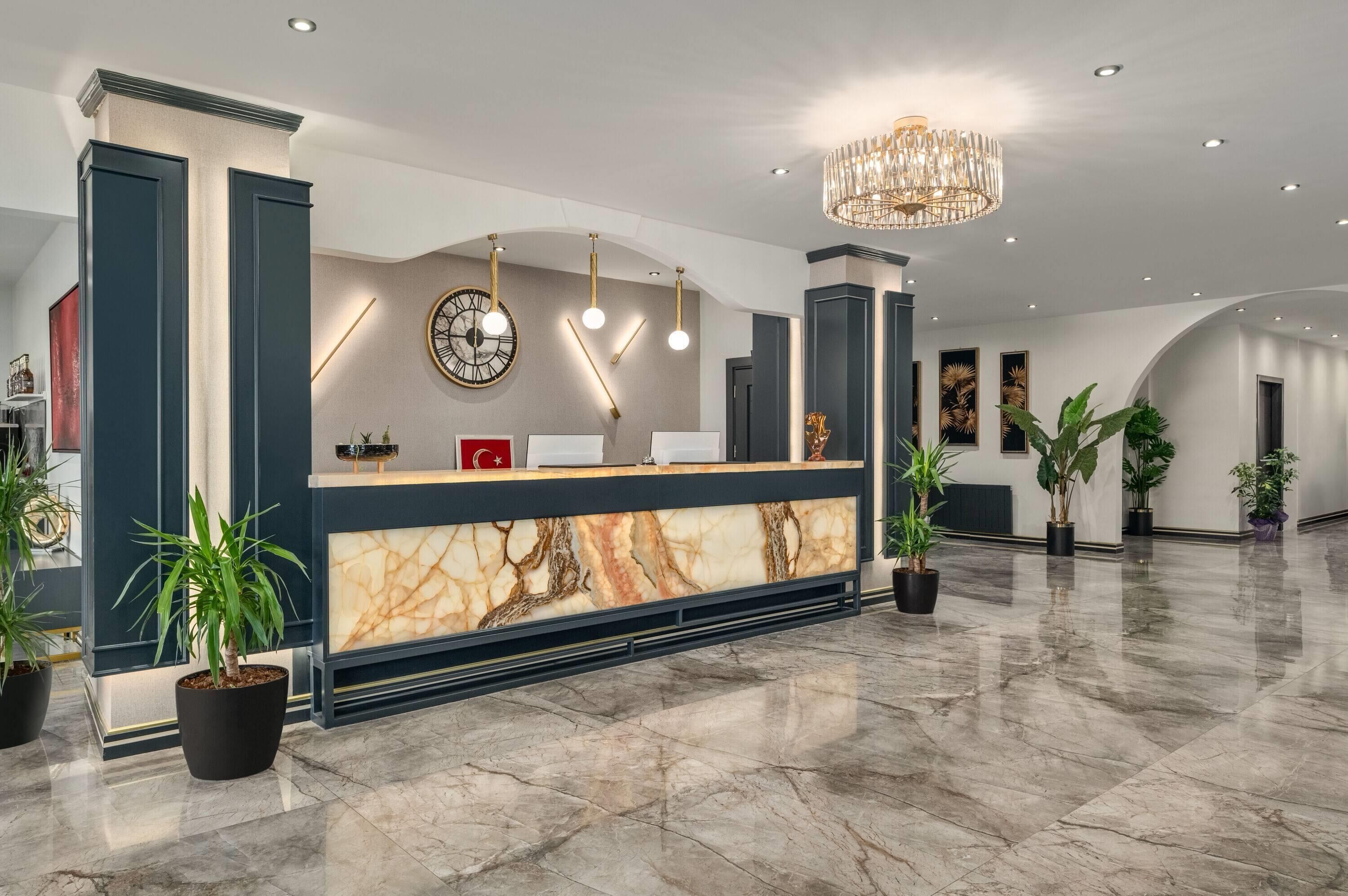 A hotel reception area with a marble counter, a clock, and a chandelier.