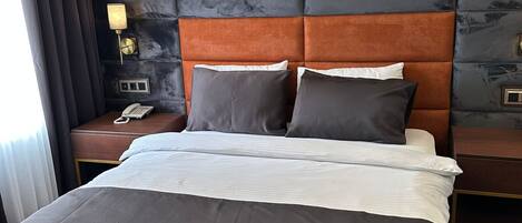 Una habitación de hotel con una cama grande, una mesita de noche con un teléfono y una lámpara de pared.