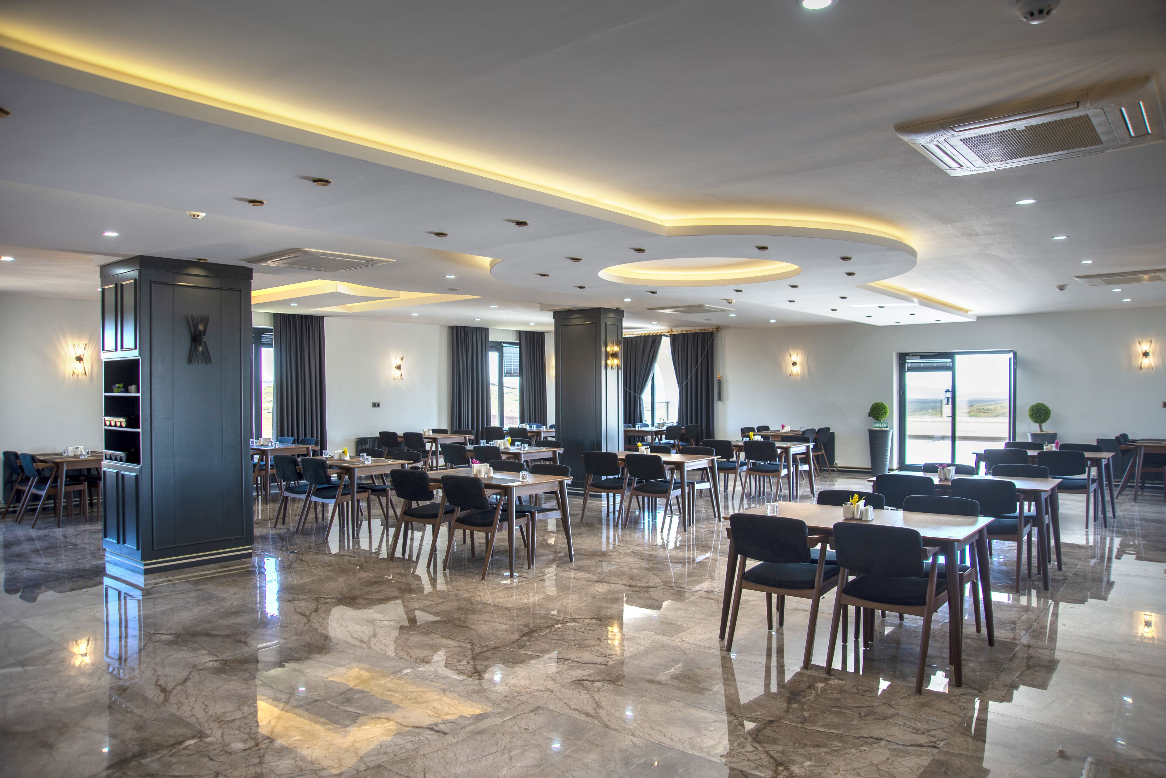 A spacious dining area with marble flooring, modern lighting, and multiple tables and chairs.