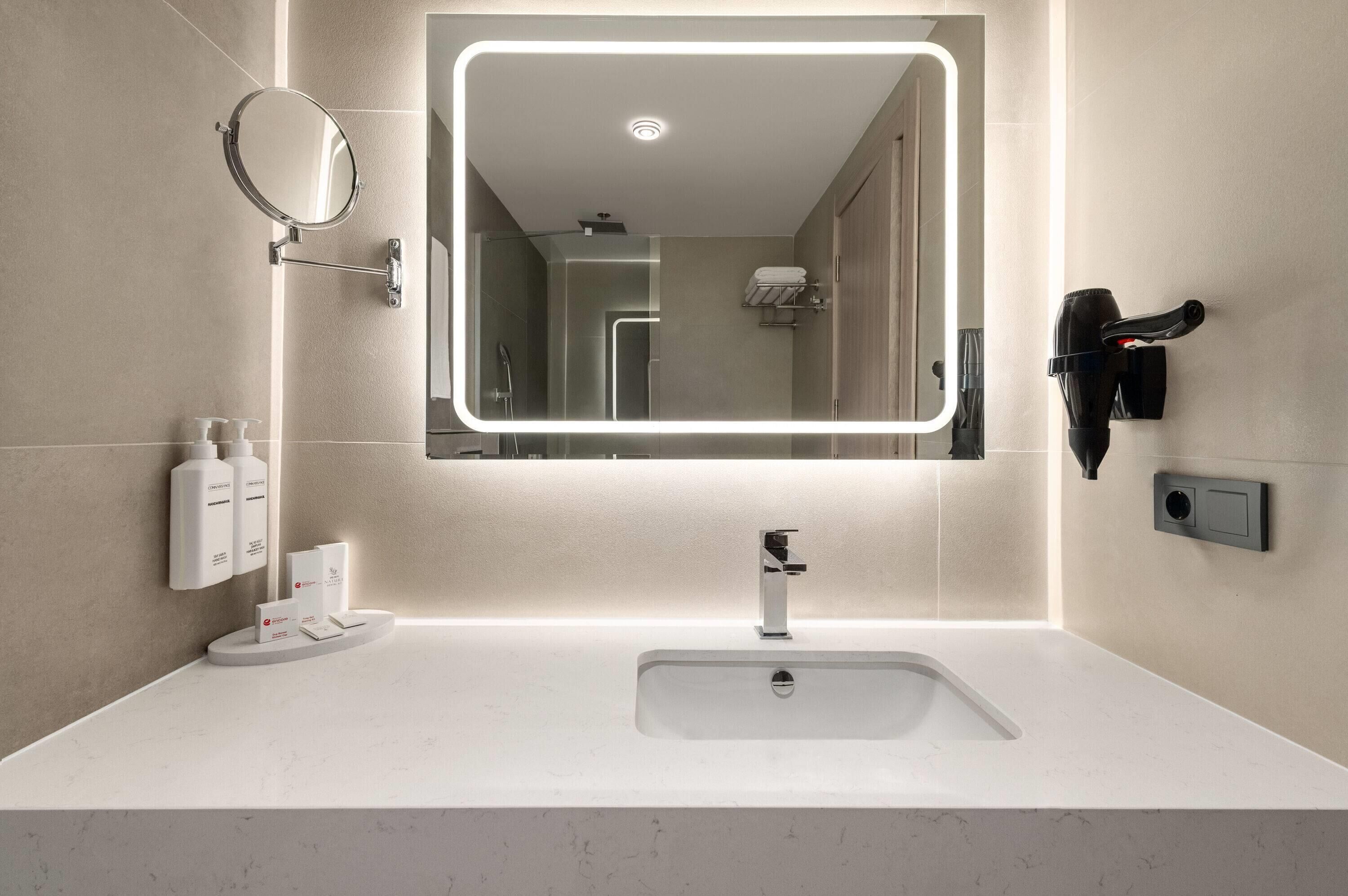 A modern bathroom with a large mirror, a sink, and a hairdryer mounted on the wall.