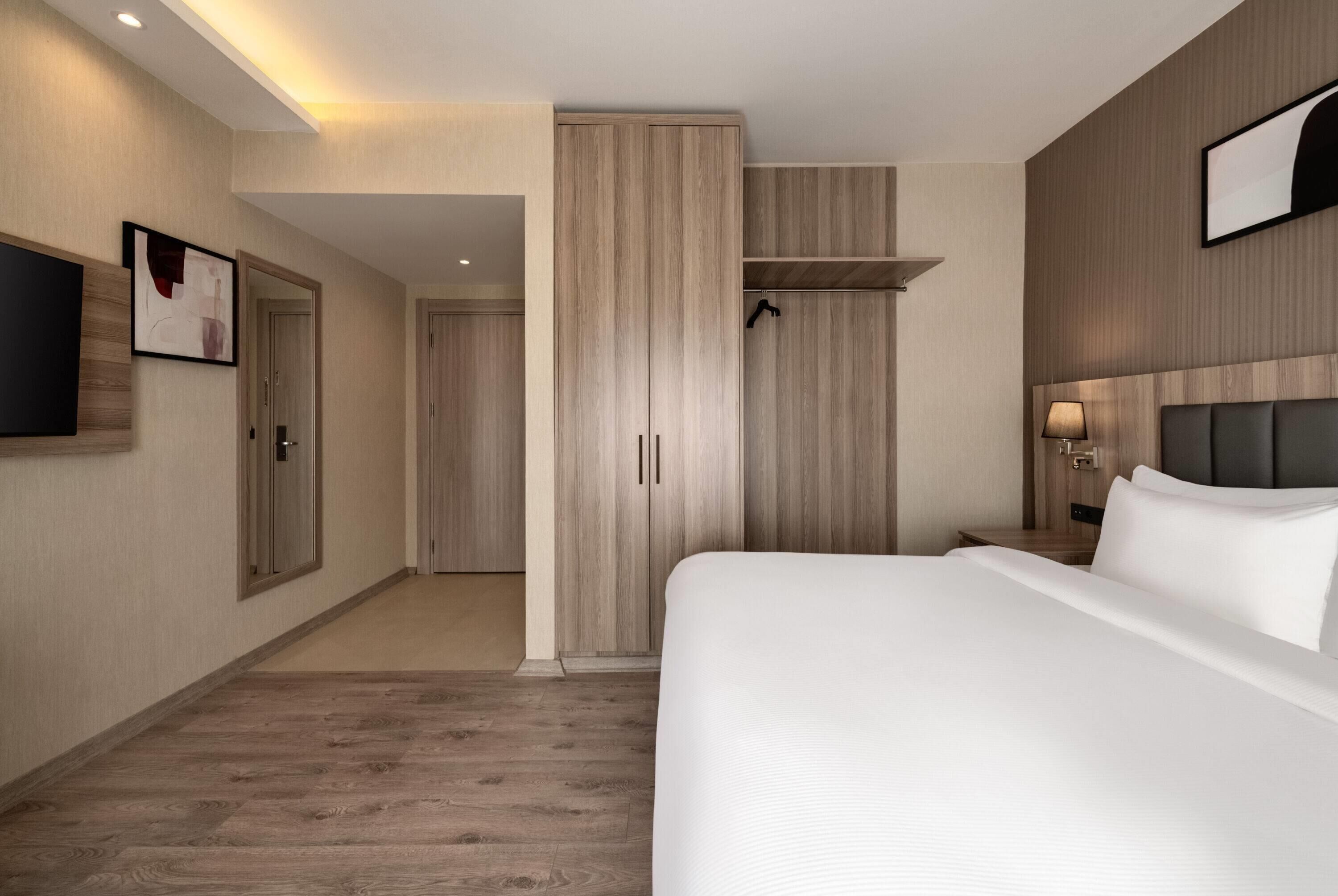 A hotel room with a large bed, a wardrobe, a television, and a bedside table with a lamp.