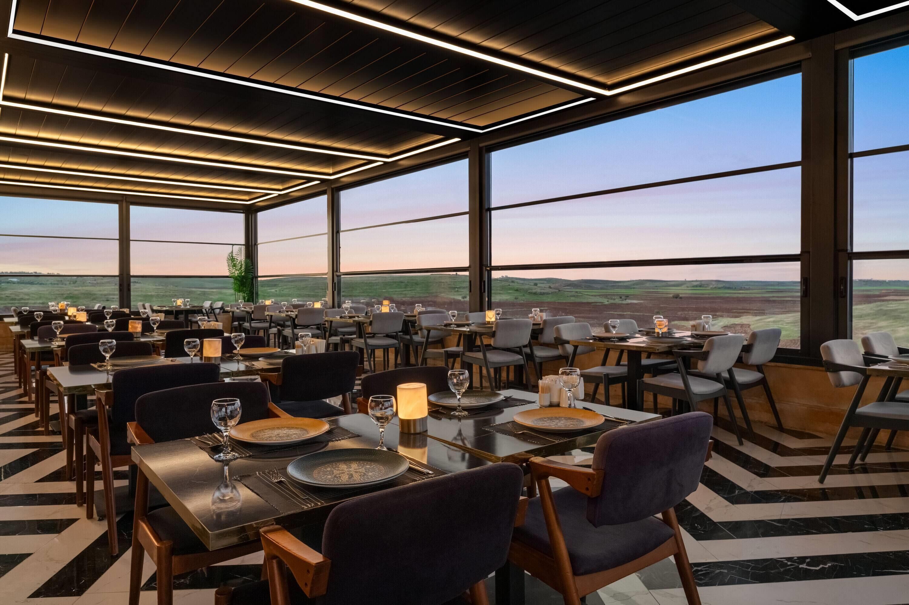 Un restaurante con vistas panorámicas al campo, que presenta un diseño interior moderno y un techo alto.