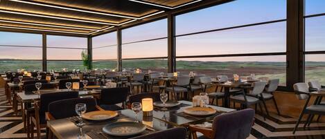 Un restaurante con vistas panorámicas al campo, que presenta un diseño interior moderno y un techo alto.