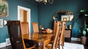 A dining room with a wooden table, six chairs, a fruit bowl, a mirror, and a potted plant.