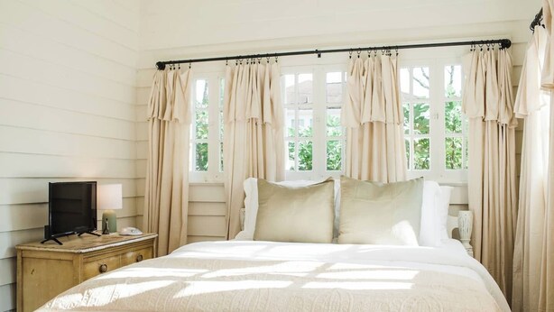 A bedroom with a bed, a nightstand, a television, and curtains.
