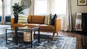 A living room with a leather sofa, a glass coffee table, a woven basket, a large clock, and a potted plant.