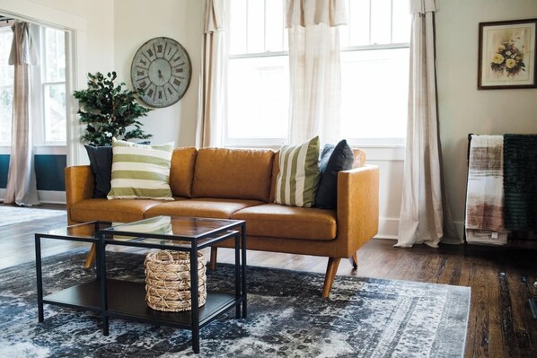 A living room with a leather sofa, a glass coffee table, a woven basket, a large clock, and a potted plant. - More than a place to stay—it's where families reconnect, sleep soundly, and create memories in a home guests can't stop talking about. (Montgomery)