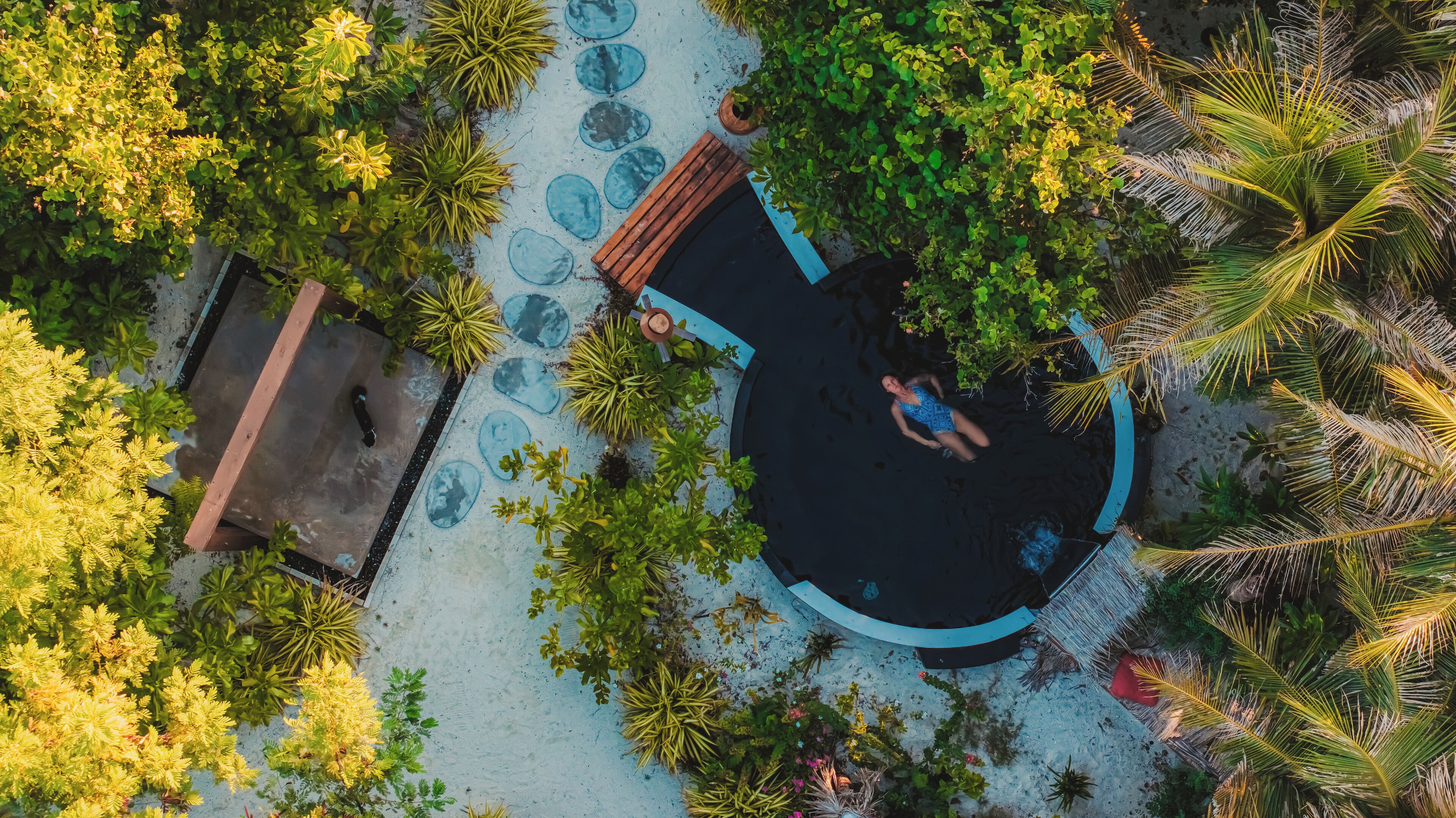Vista aérea de uma piscina circular cercada por vegetação exuberante e palmeiras.