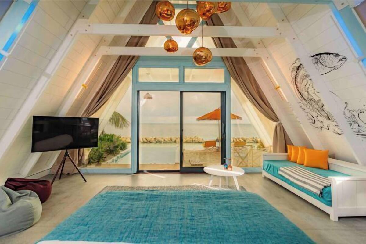 A modern living room with a large TV, a sofa, a coffee table, and a view through a glass door to an outdoor area.