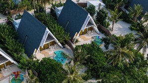 An aerial view of a resort with multiple bungalow-style buildings, a central swimming pool, and lush tropical vegetation. - Oaga Art Resort (Maaranfushi)