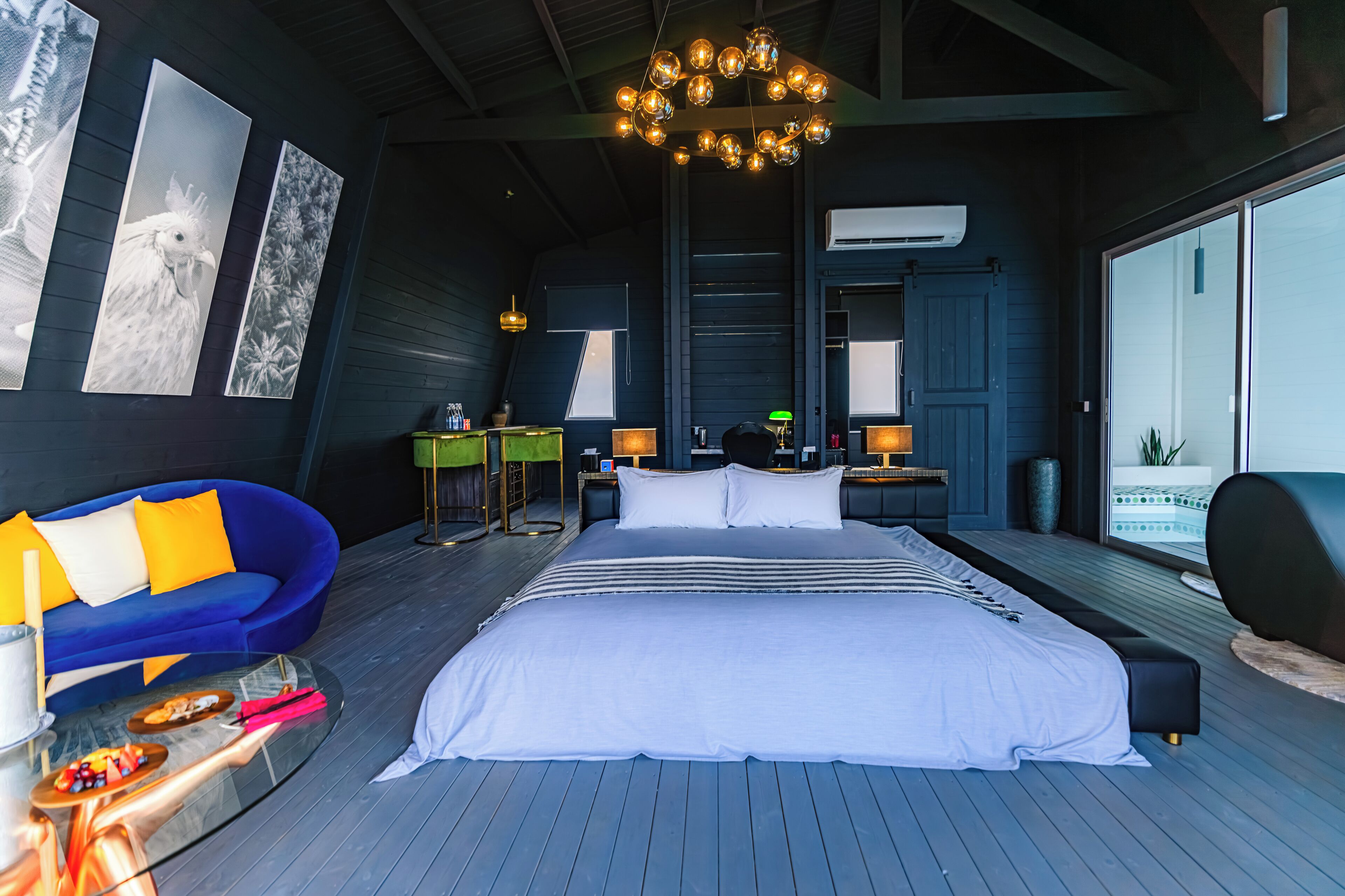 A modern bedroom with a large bed, a blue sofa, a desk, and a view of the outdoors.