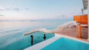 A pool area with a slide, wooden deck, and a view of the ocean. - Oaga Art Resort (Maaranfushi)