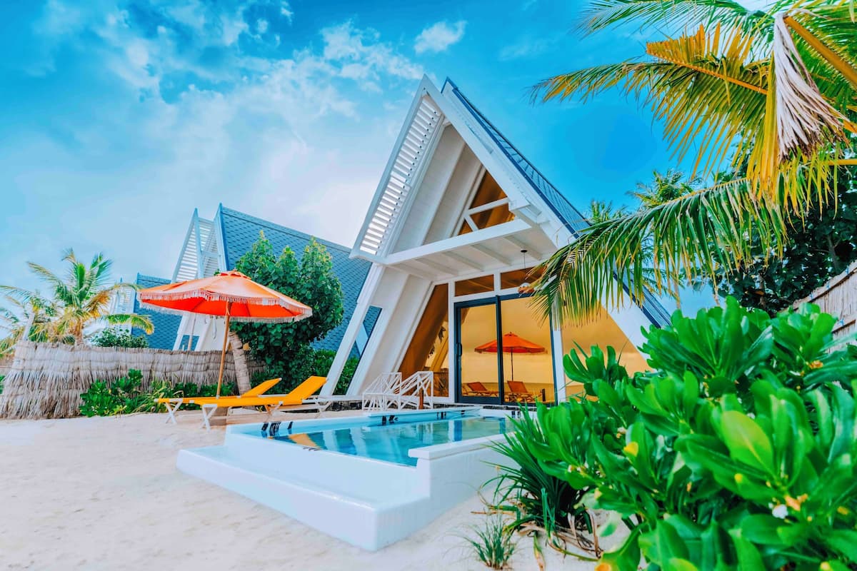 A modern hotel with a pool, sun loungers, and palm trees.