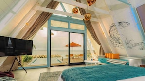 A bedroom with a large bed, a TV, and a balcony with a view of the beach.
