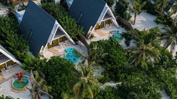 Eine Vogelperspektive zeigt ein Resort mit mehreren bungalowsartigen Gebäuden, einem zentralen Schwimmbecken und üppiger tropischer Vegetation.