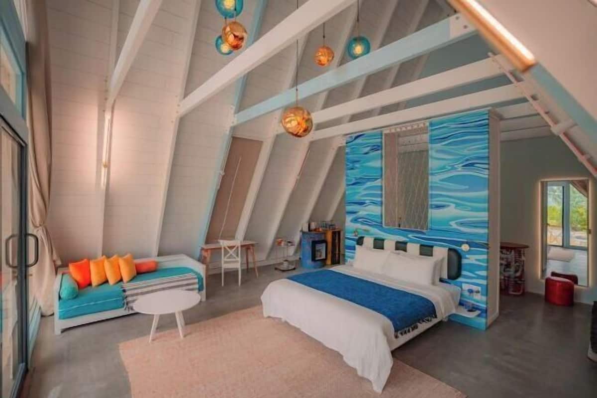 A bedroom with a bed, a sofa, a small table, and a wall with a blue abstract design.