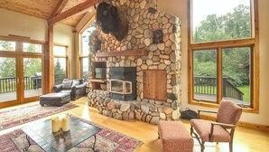 Una sala de estar amplia con chimenea de piedra, ventanas grandes y un rincón de estar acogedor.