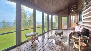 Una terraza de madera con una mesa y sillas, ventanas amplias y vistas al exterior.