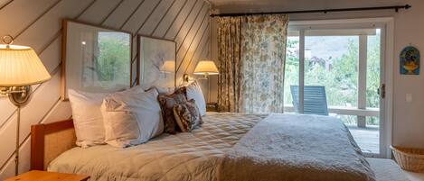 A bedroom with a large bed, two bedside lamps, a wooden nightstand, and a view of the outdoors through a sliding glass door.