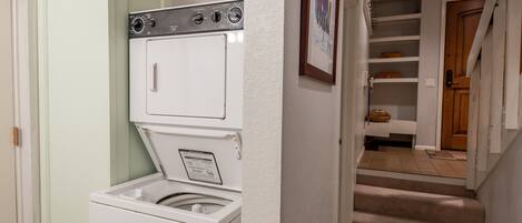 A laundry room with a front-loading washer and dryer, a wicker basket on top of the dryer, and a framed picture on the wall.