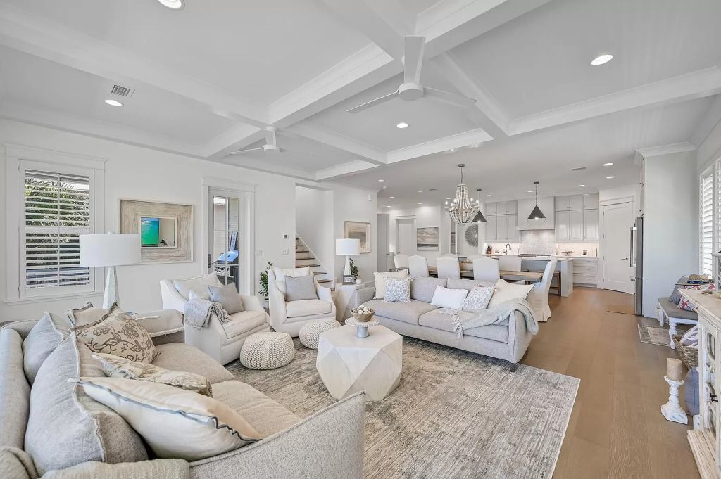 A spacious living room with a neutral color palette, a large sofa, a coffee table, and a kitchen area in the background.