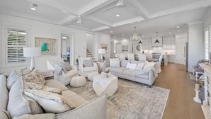A spacious living room with a neutral color palette, a large sofa, a coffee table, and a kitchen area in the background.