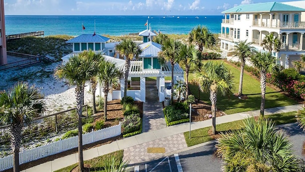 A coastal hotel with a beach view, palm trees, and a clear sky.