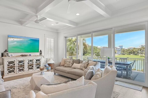 A spacious living room with a large flat-screen TV, a beige sofa, and a dining area with a view of a golf course.