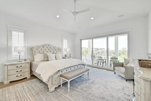 A spacious bedroom with a large bed, a bench, a nightstand, and a view of the outdoors through large windows.