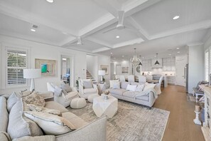 A spacious living room with a neutral color palette, a large sofa, a coffee table, and a kitchen area in the background.